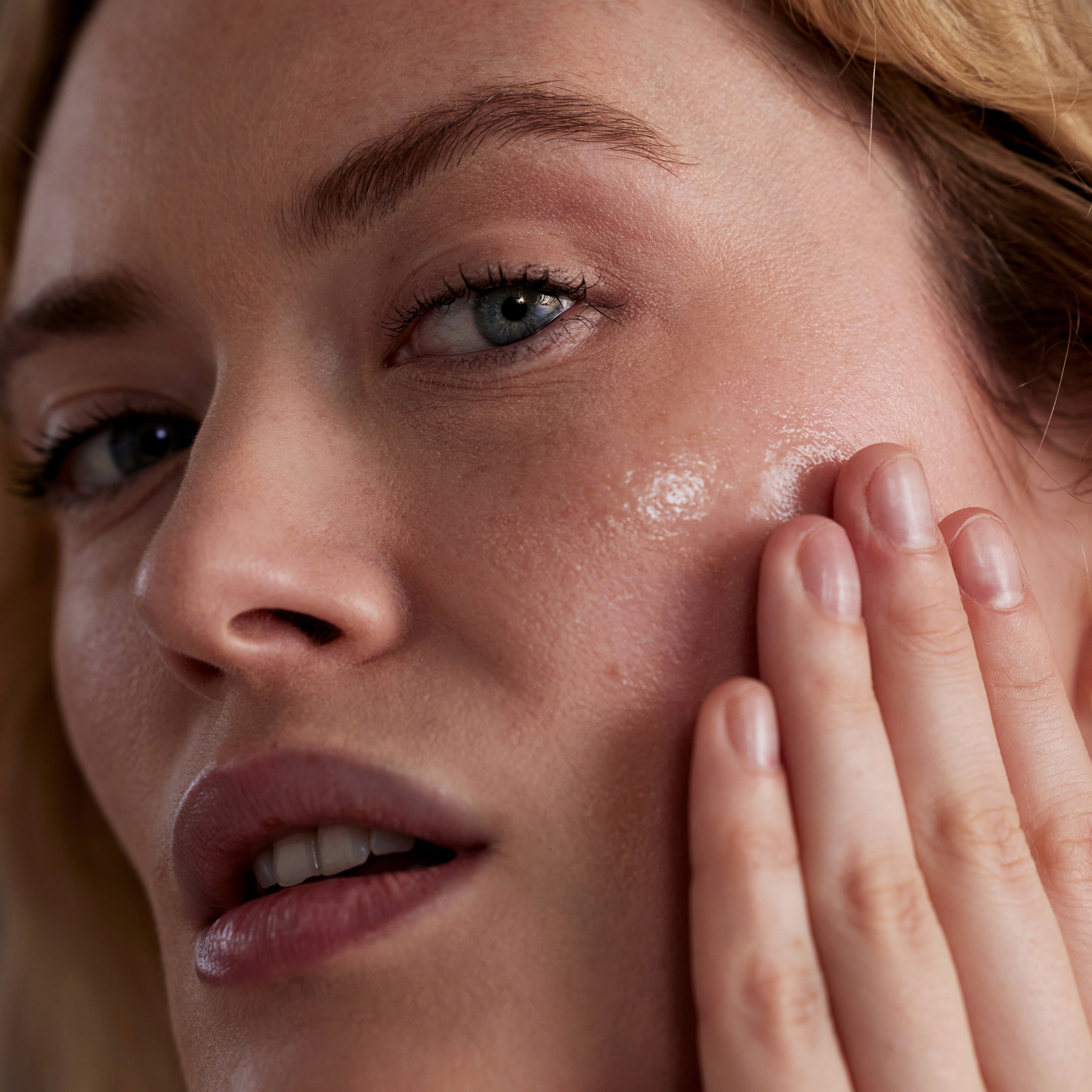 Woman smiling as she applies skin products to her face